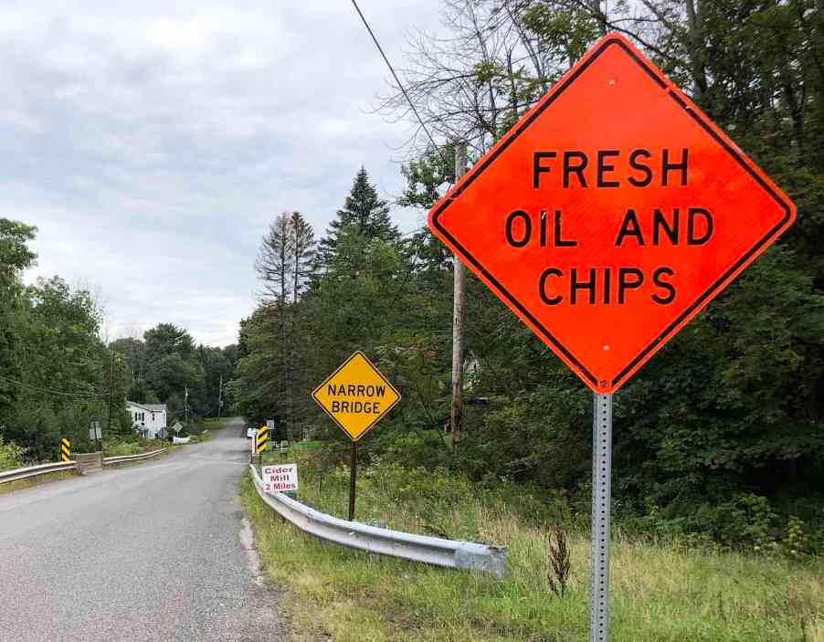 Bright orange "Fresh Oil and Chips" construction sign on a refinished country road.