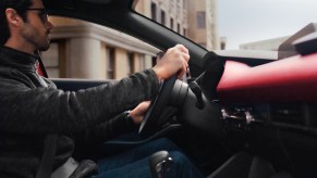 Man holding the steering wheel of a Mazda 3 sports sedan with a red interior