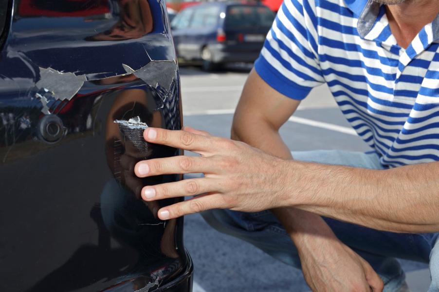 Man points at a dented rear bumper from a crash while parallel parking.