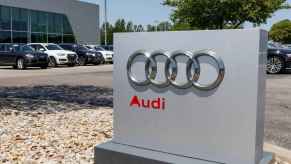 The exterior sign of an Audi dealership with Audi vehicles parked in a row behind