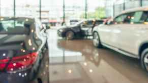 A blurred image of the showroom floor at a car dealership with shiny floor and several new cars