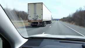 The right rear view of a semi-truck from the left front corner of the dash of a car on a highway