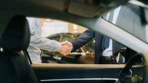 Two men shaking hands view from inside car interior at a dealership