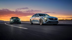 Two Cadillac sedans drive on a race track, the sunset behind them.