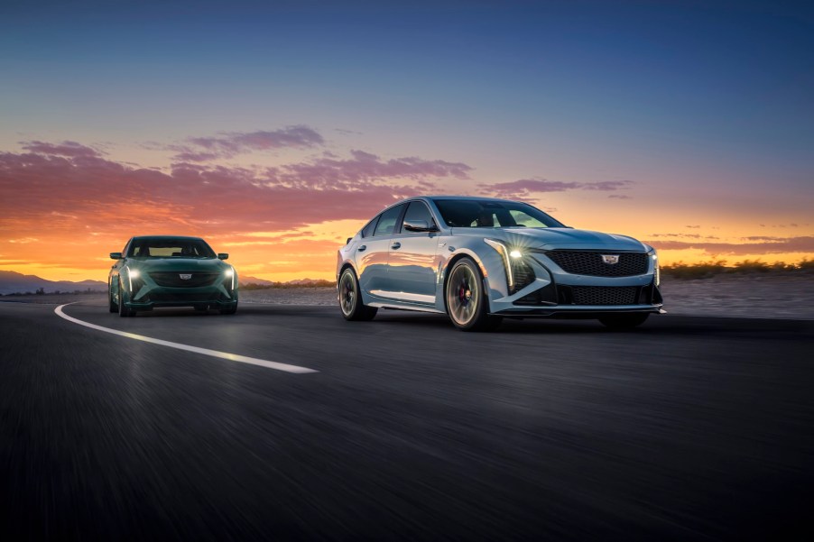 Two Cadillac sedans drive on a race track, the sunset behind them.