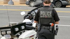 A police officer walks up to their motorcycle in body armor.