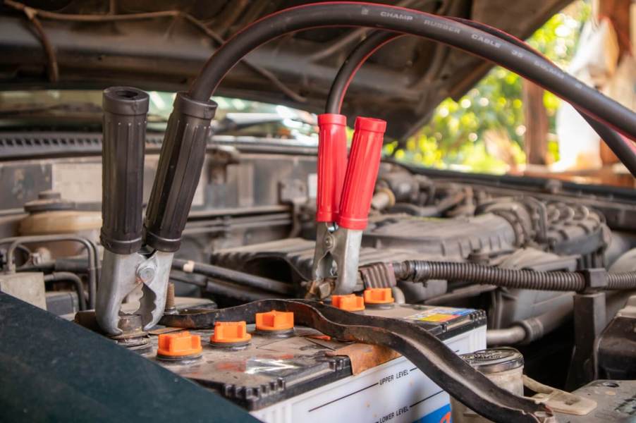 A car owner jumps a battery with a set of jumper cables.