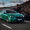 A green 2025 BMW M5 drives around a corner.