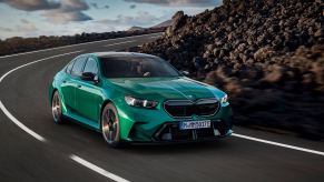 A green 2025 BMW M5 drives around a corner.