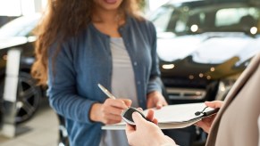 Woman signs a rental car contract as she's handed the keys, in a parking lot.