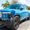 blue electric Rivian truck plugged into a charging cable.