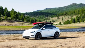 A white Tesla Model Y with a roof rack and surfboards out in nature.