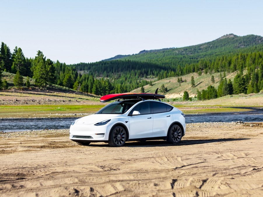 A white Tesla Model Y with a roof rack and surfboards out in nature.