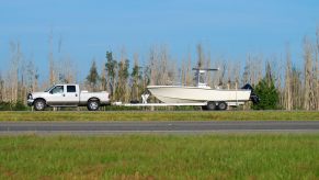 A white truck towing a trailer with a boat.