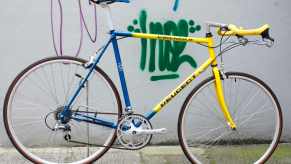 Vintage blue and yellow Peugeot road racing bicycle leaned against a graffiti-covered wall.