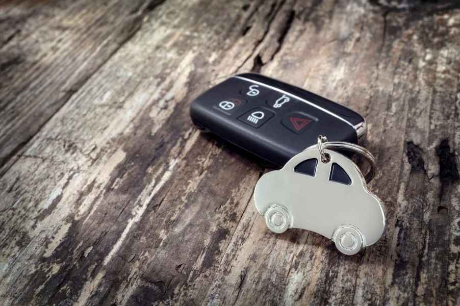 A black car key fob with a silver metal car cutout keychain sitting on a distressed wood surface