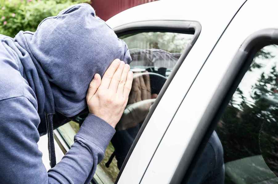 man in blue hoodie face covered peering into car window in close view hand covering side of face depicting car theft