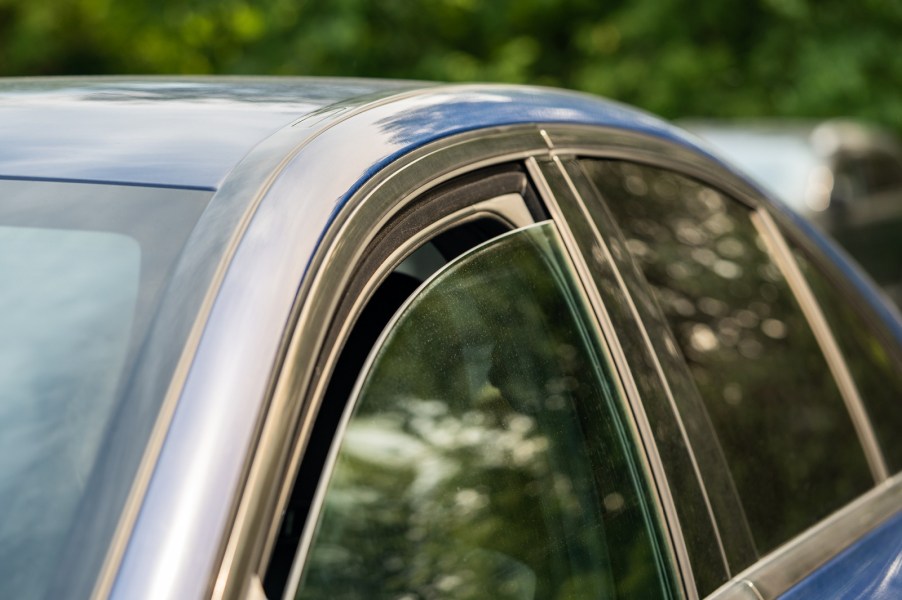 Left front window of a blue car rolled down a small amount some people only open their windows slightly at a traffic stop