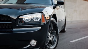 A black Dodge Charger muscle car parked on a paved road in left front angle view showing the left front corner