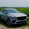 Gray crossover SUV with a coupe fastback parked in a field, trees visible in the background.