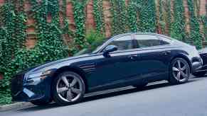 Dark green Genesis luxury sedan parked in front of a vine covered wall.