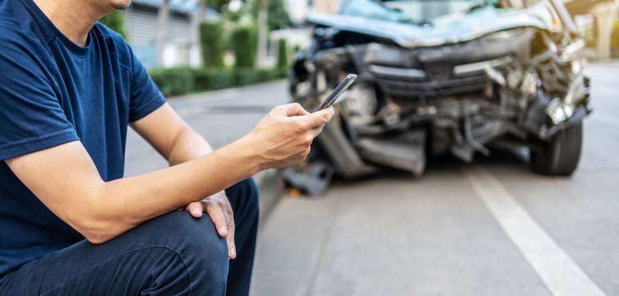 Driver sits next to a crashed car while making a phone call.