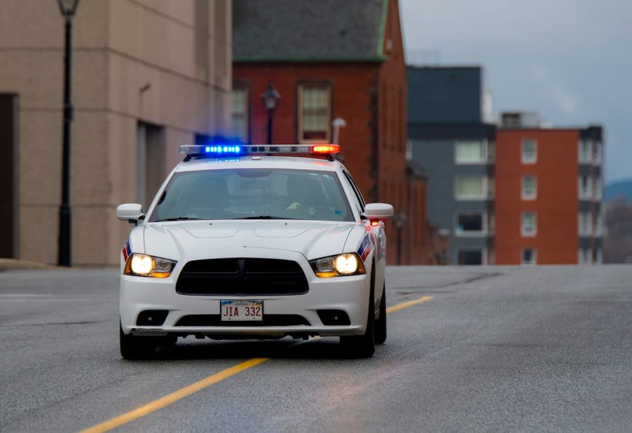 A white municipal Dodge Charger police car flashes its lights before participating in a high-speed chase.