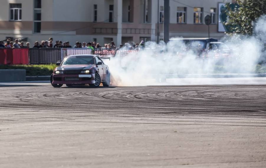 A Nissan drift car slides in a cloud of smoke in front of spectators.