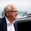 Governor Tim Walz stands in front of a black SUV.