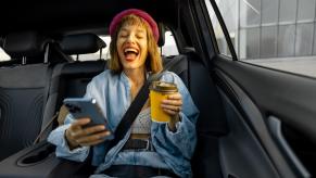 A person laughs in a car as ChatGPT AI roasts cars on their phone.