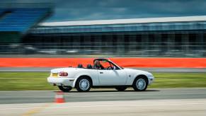 An NA Mazda MX-5 Miata drives around a track like the Nürburgring or Silverstone.