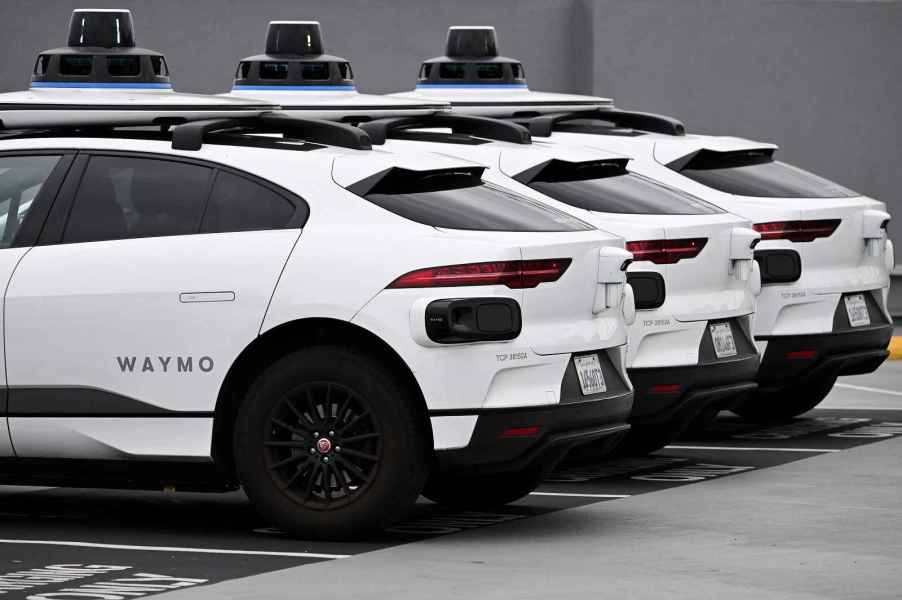 Three white Waymo driverless cars parked in a lot in a row