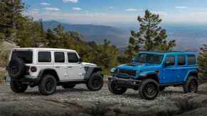 Two 2023 Jeep Wrangler SUVs parked on a gravel mountain trail facing each other in profile view