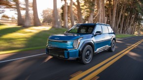 A blue 2024 Kia EV9 driving on a road in left front angle view