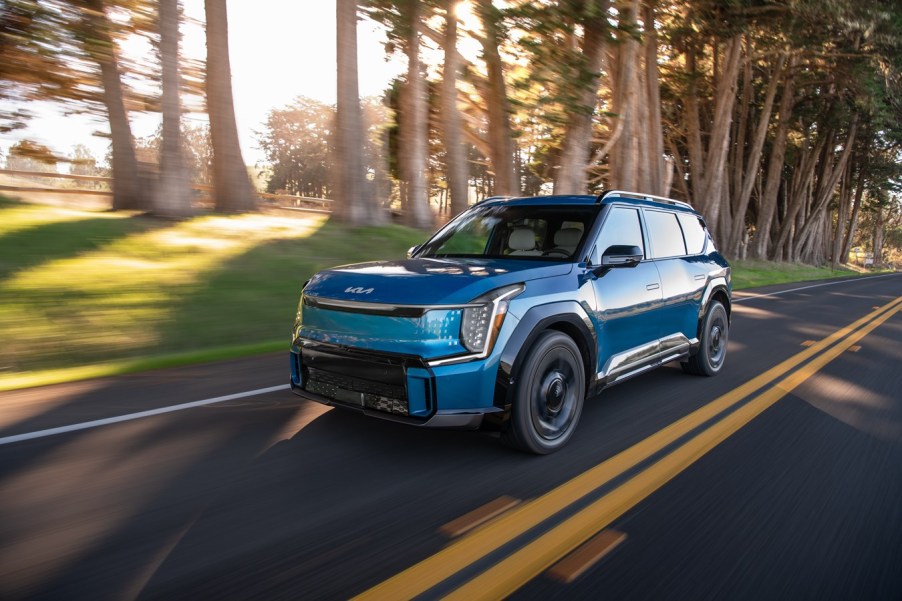 A blue 2024 Kia EV9 driving on a road in left front angle view