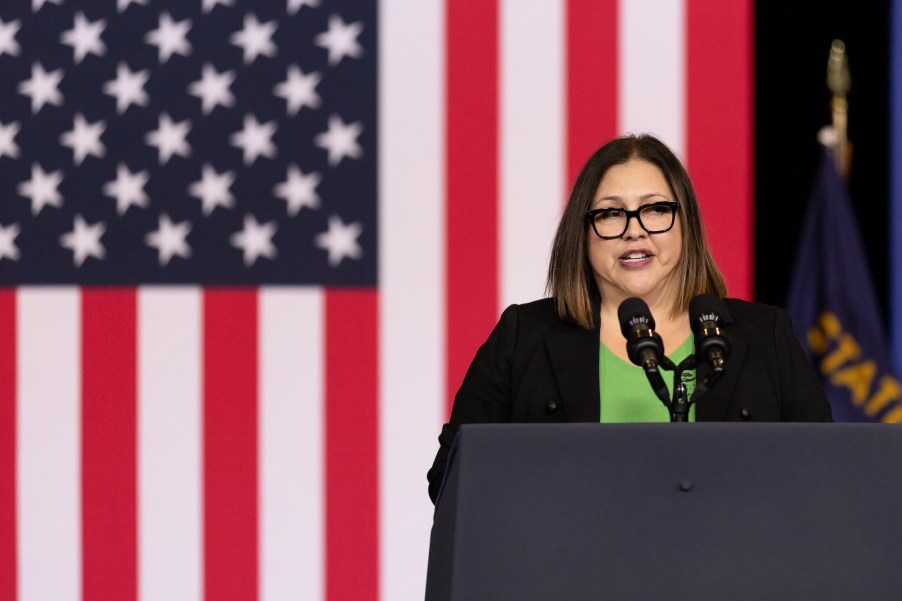 Portland Oregon mayor hopeful Carmen Rubio speaks into a microphone at a podium, an American flag behind her