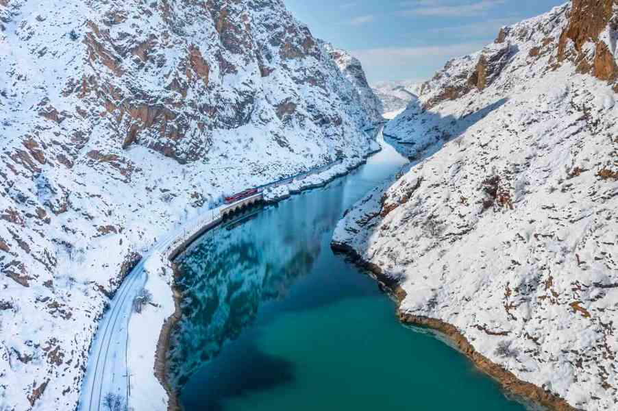 The eastern orient express navigates a narrow mountain valley in Turkey, alongside a river.