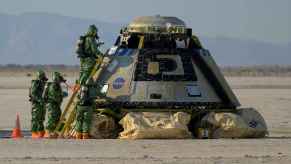 The Boeing Starliner landing in New Mexico in 2022 after an unmanned flight test with NASA staff wearing green hazmat suits outside the craft