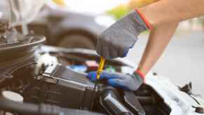 Gloved technician checking a car's engine oil level pulling the dipstick before an oil change in close view