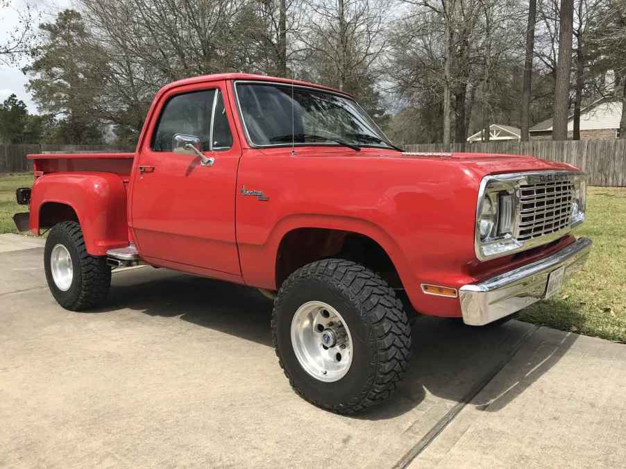 A red 1976 classic Dodge W100 pickup truck parked outside on cement in low right front angle view