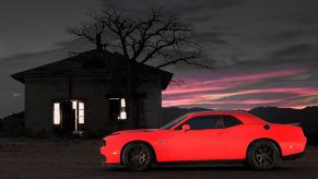 A bright red Dodge Challenger SRT Hellcat and its thirsty supercharger with a horsepower need beyond a Mitsubishi Mirage at night.