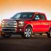 A red 2015 Ford F-150 parked in full left front angle view with sun setting in background