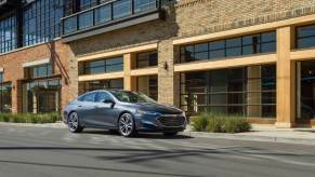 A gray Chevrolet Malibu parked alongside a large building.