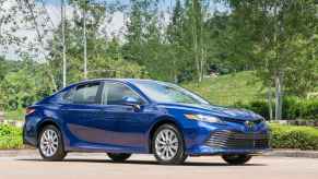 A metallic blue 2019 Toyota Camry parked in full right front angle view with green hills and trees in background