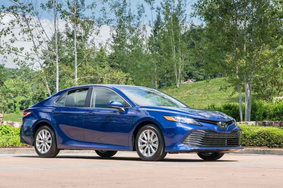 A metallic blue 2019 Toyota Camry parked in full right front angle view with green hills and trees in background