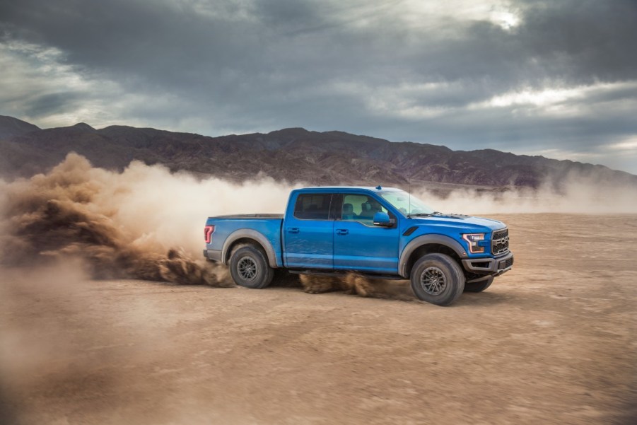 A blue 2020 Ford F-150 driving and kicking up dust in a desert environment