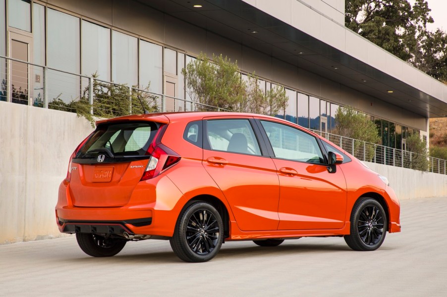 A dark orange 2020 Honda Fit parked in right rear angle view in front of a building with large glass windows