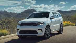 A white 2024 Dodge Durango SUV parked in left front angle view in front of mountains and cloudy blue sky