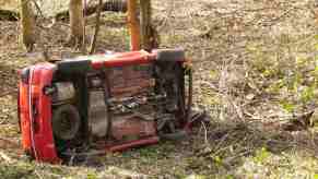 Bright red car on its side in the woods after a crash.