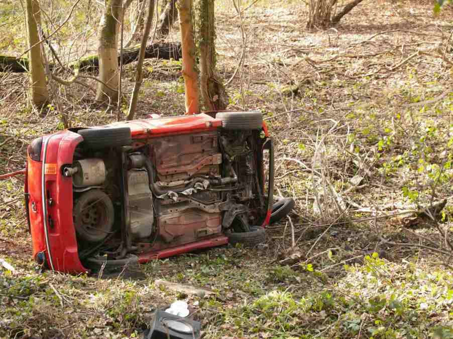 Bright red car on its side in the woods after a crash.